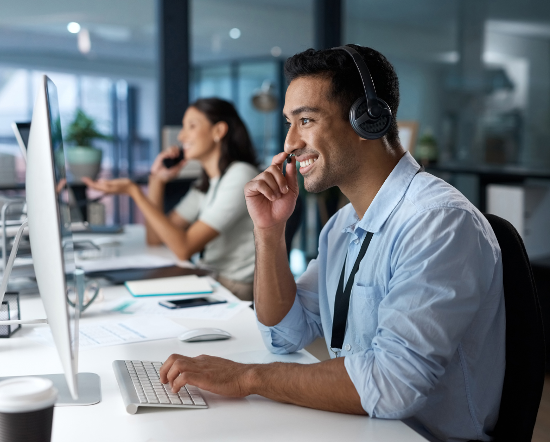 a tech support man sitting at a desk talking on the phone while looking at his computer monitor